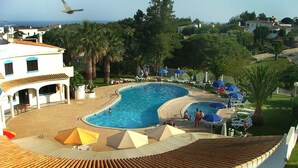 Una amplia piscina exterior con tumbonas y sombrillas, rodeada de palmeras y vista al mar.