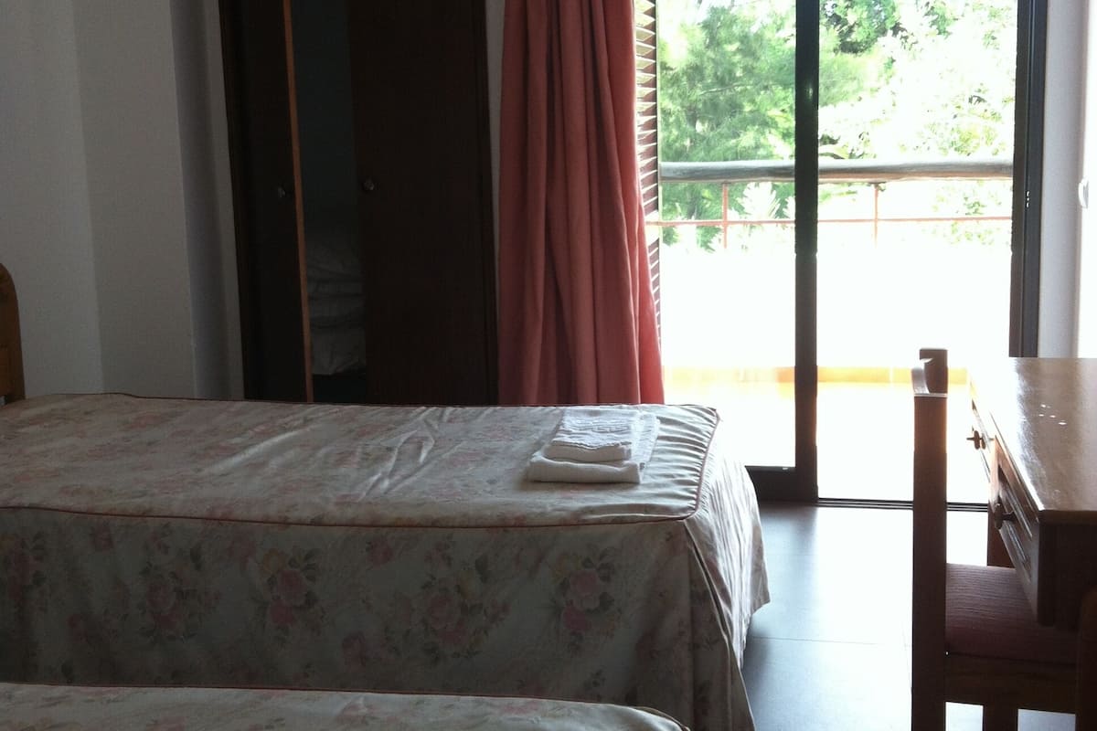 A room with two beds, a desk, and a sliding glass door leading to an outdoor area.
