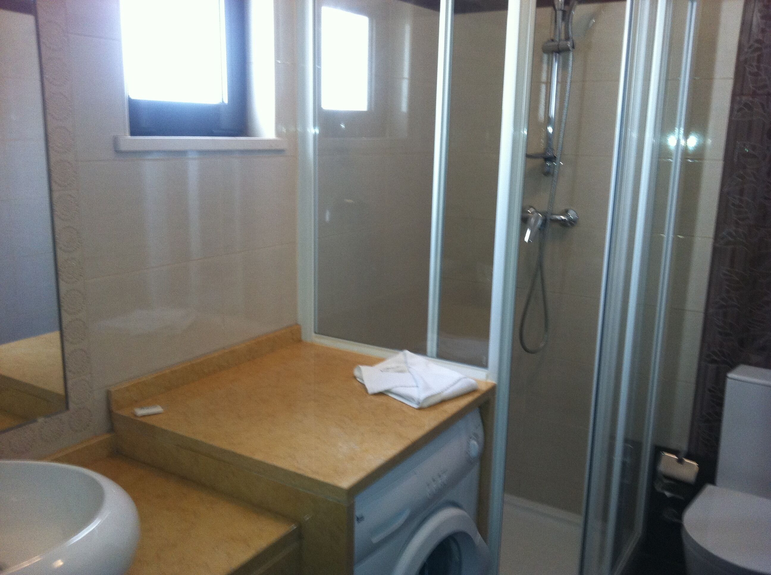 A bathroom with a glass-enclosed shower, a sink, and a washing machine.