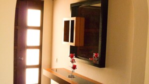 Un pasillo con techo de madera, una puerta con ventanal, un espejo y una pequeña mesa con un jarrón de rosas rojas.