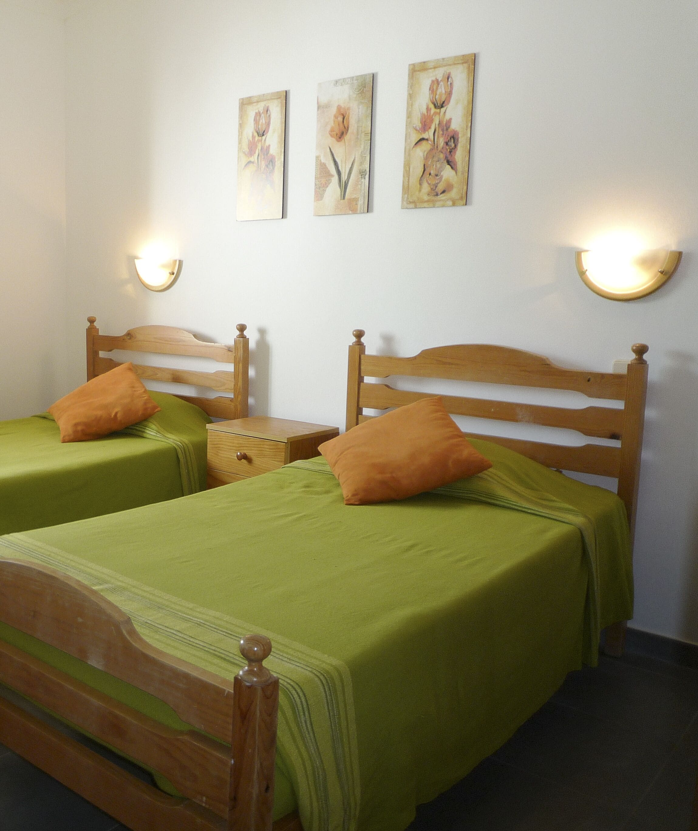 Une chambre avec deux lits en bois, une literie verte et des luminaires fixés au mur.
