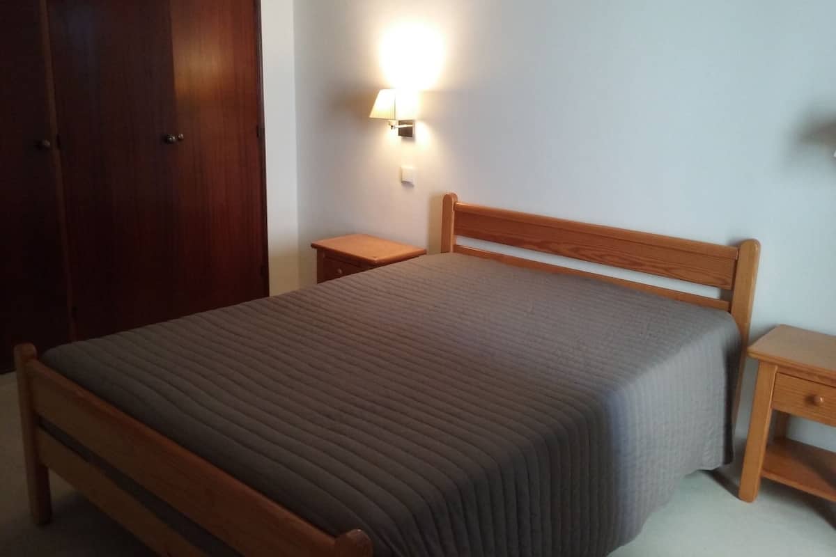 A bedroom with a wooden bed, a nightstand, a wall-mounted lamp, and a wardrobe.