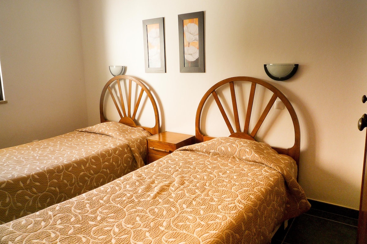 A twin room with two single beds, a bedside table, a wall-mounted shelf, and a mirror.