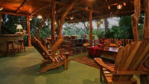 Una terraza de madera al aire libre con mobiliario rústico, que incluye sillas de madera y una mesa de comedor, rodeada de abundante follaje.