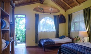 Une chambre avec deux lits, un plafond en bois, une grande fenêtre avec des rideaux et une porte donnant sur l’extérieur.