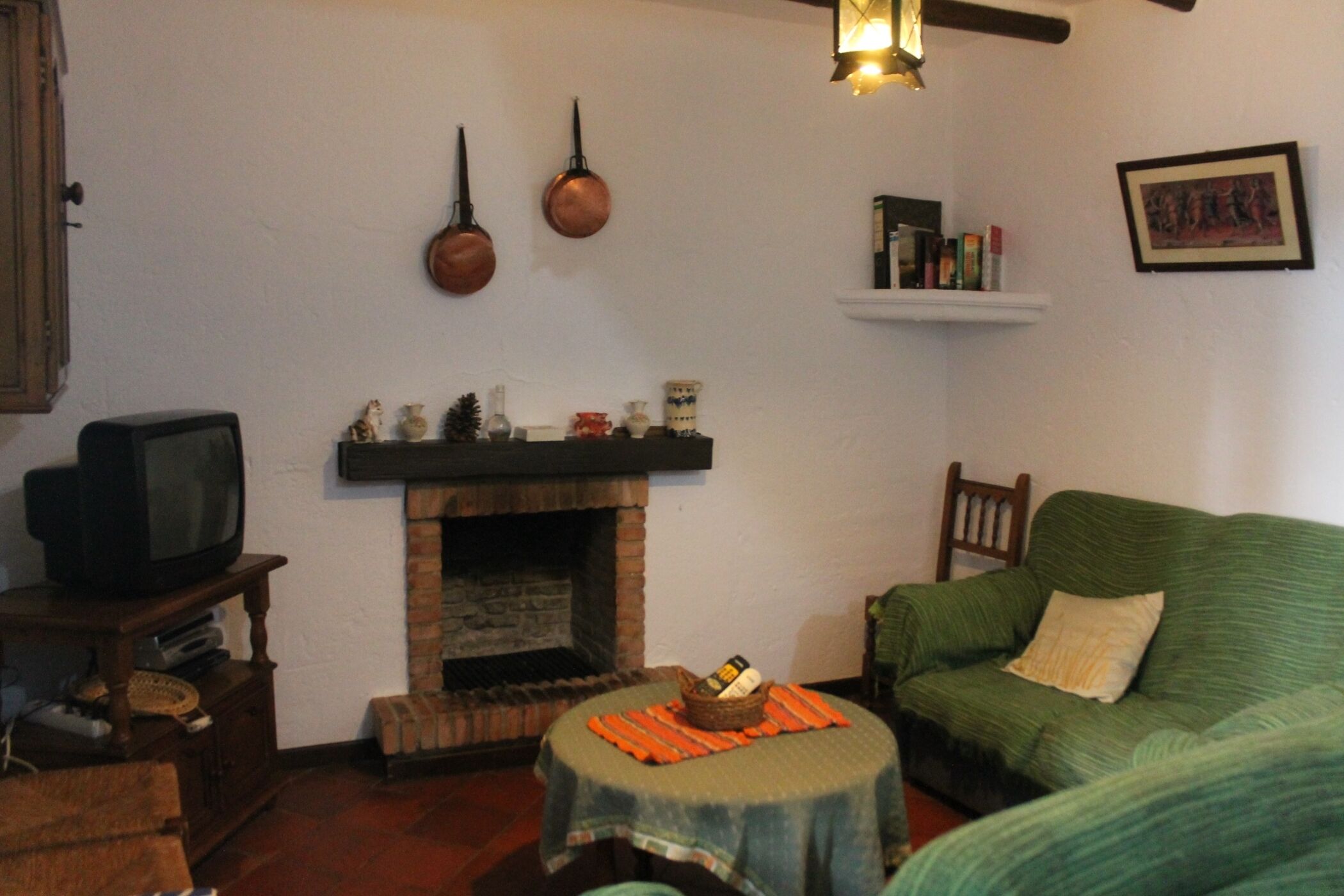 Un salon chaleureux avec une cheminée, un téléviseur posé sur un meuble en bois, un canapé vert et une petite table avec un set de table.