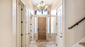 A hallway with a wooden door, a chandelier, and a carpeted floor.