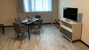 Een moderne kamer met een eettafel, stoelen, een televisie op een kast en een raam met gordijnen.