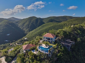 A large house with a swimming pool, surrounded by lush green hills.