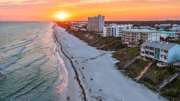 Un hotel frente a la playa con varias construcciones, una playa de arena y el océano.