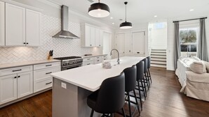 Una cocina moderna con armarios blancos, una isla central con taburetes y lámparas colgantes.