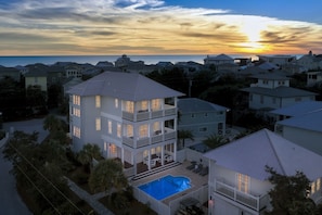 A multi-story house with a pool and a view of the ocean at sunset.