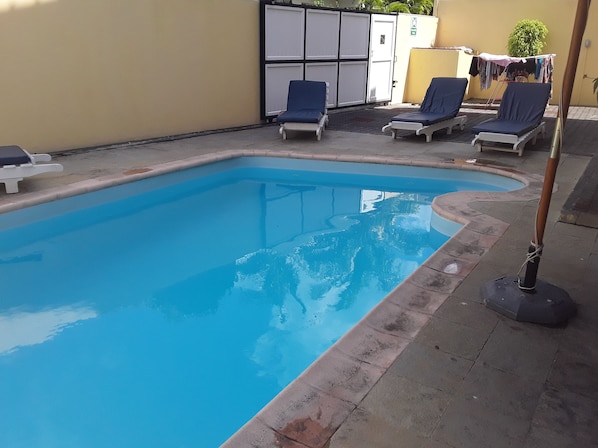 A rectangular swimming pool with a tiled edge, surrounded by lounge chairs and a small garden area with a clothesline.