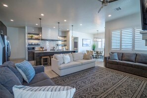 A modern living room with a grey sofa, a patterned rug, and a kitchen area with a dining table and chairs.