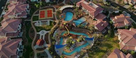 An aerial view of a resort with multiple swimming pools, a water slide, and a tennis court.