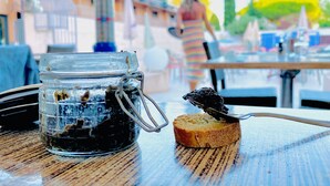 Un bocal en verre avec un fermoir en métal, posé sur une table en bois, une tranche de pain tartinée et une cuillère.