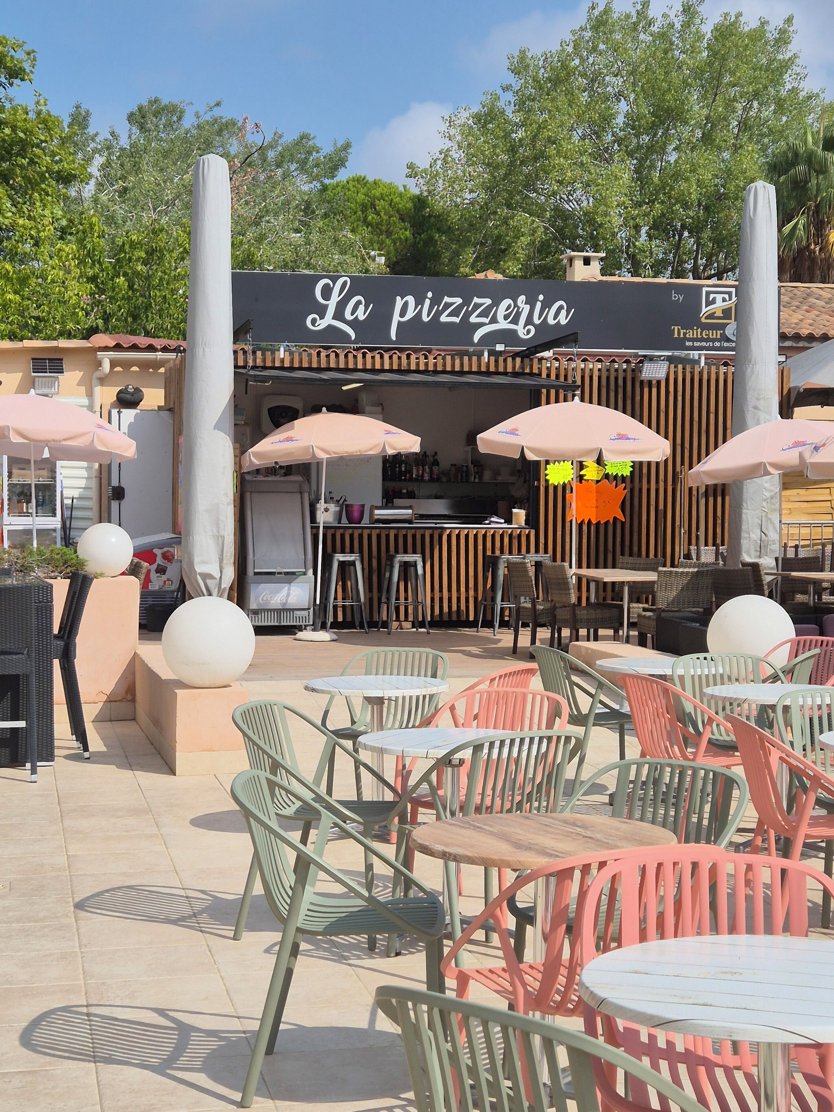 An outdoor seating area with tables and chairs, a pizzeria sign, and a wooden fence.