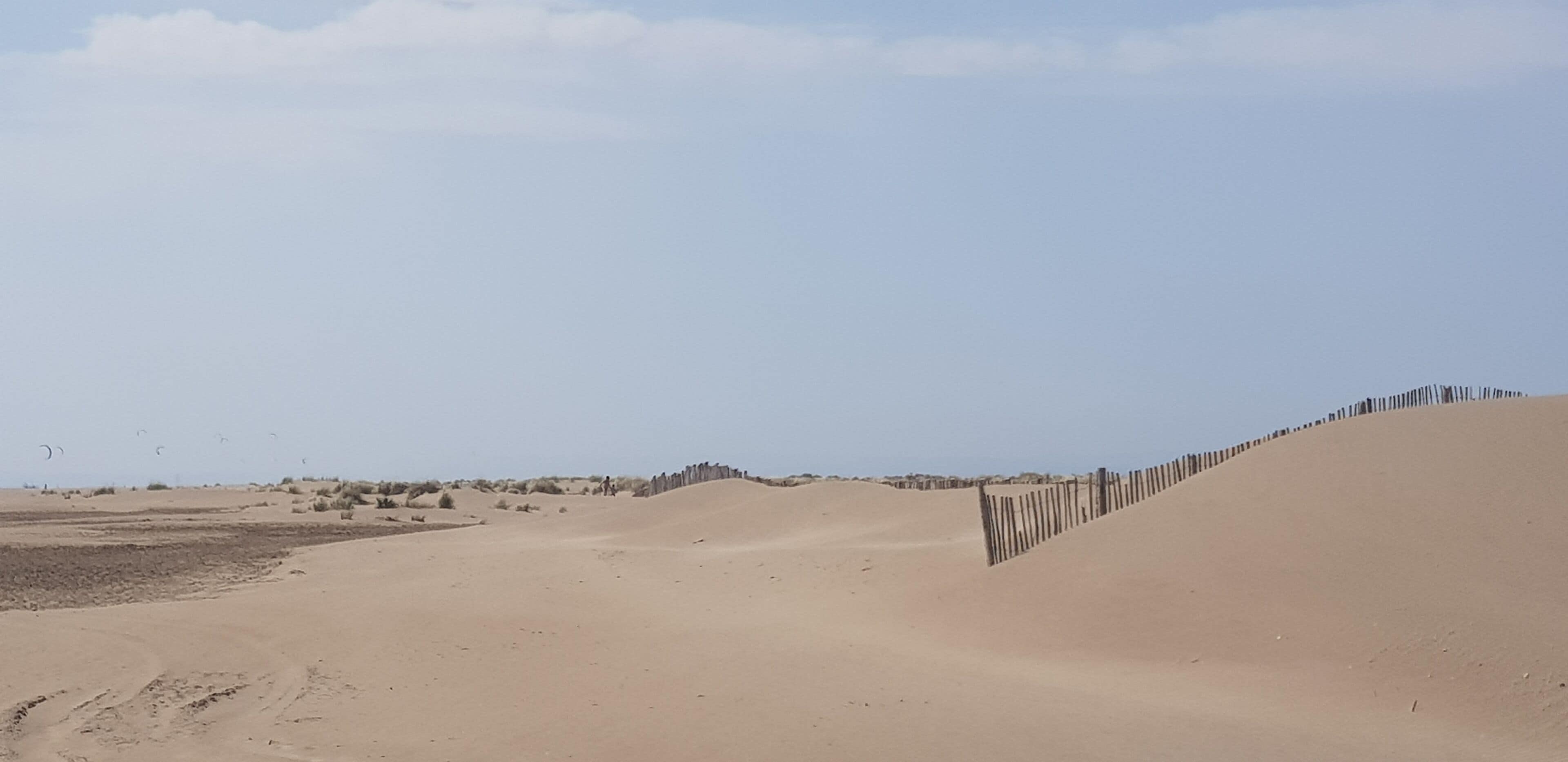 Wüstenlandschaft mit Sanddünen und einem Holzzaun.