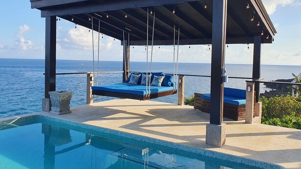 A poolside area with a swing chair and a covered seating area overlooking the sea. - West Bay Suite  (King Suite) (West Bay)