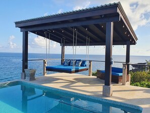 A poolside area with a swing chair and a covered seating area overlooking the sea. - West Bay Suite (King Suite) (West Bay)