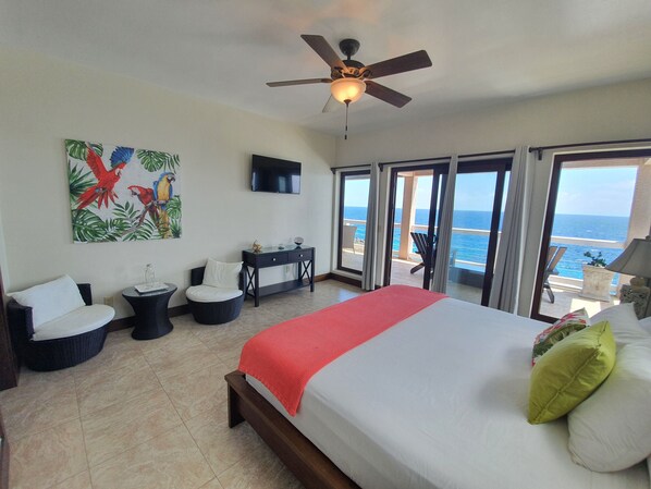 A bedroom with a bed, a ceiling fan, a TV, a desk, and a view of the ocean. - West Bay Suite (King Suite) (West Bay)