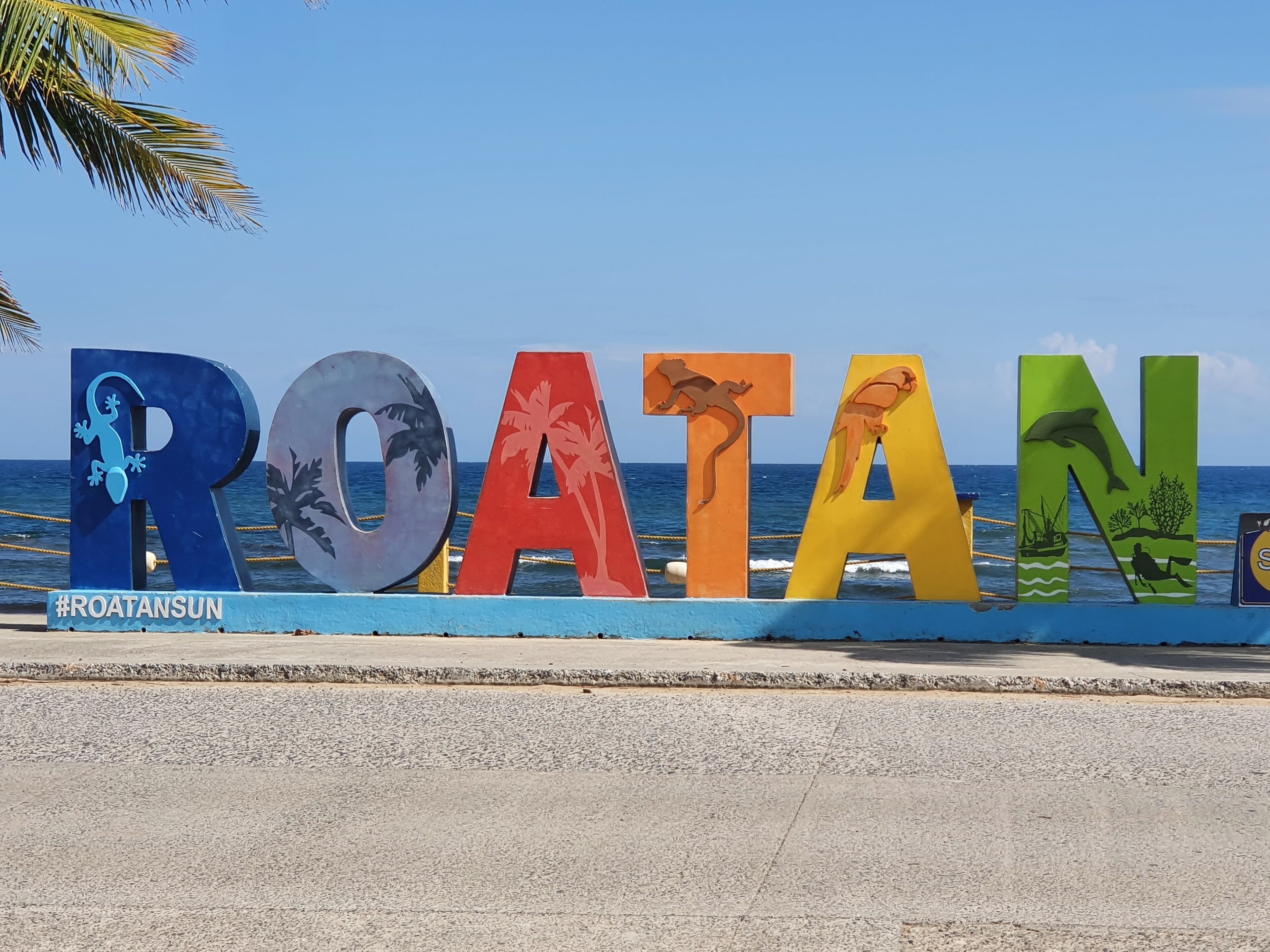 Une enseigne colorée sur laquelle est écrit « ROATAN » et qui présente divers motifs d’animaux et de plantes.