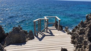 A wooden deck leading to a rocky coastline with a view of the ocean.