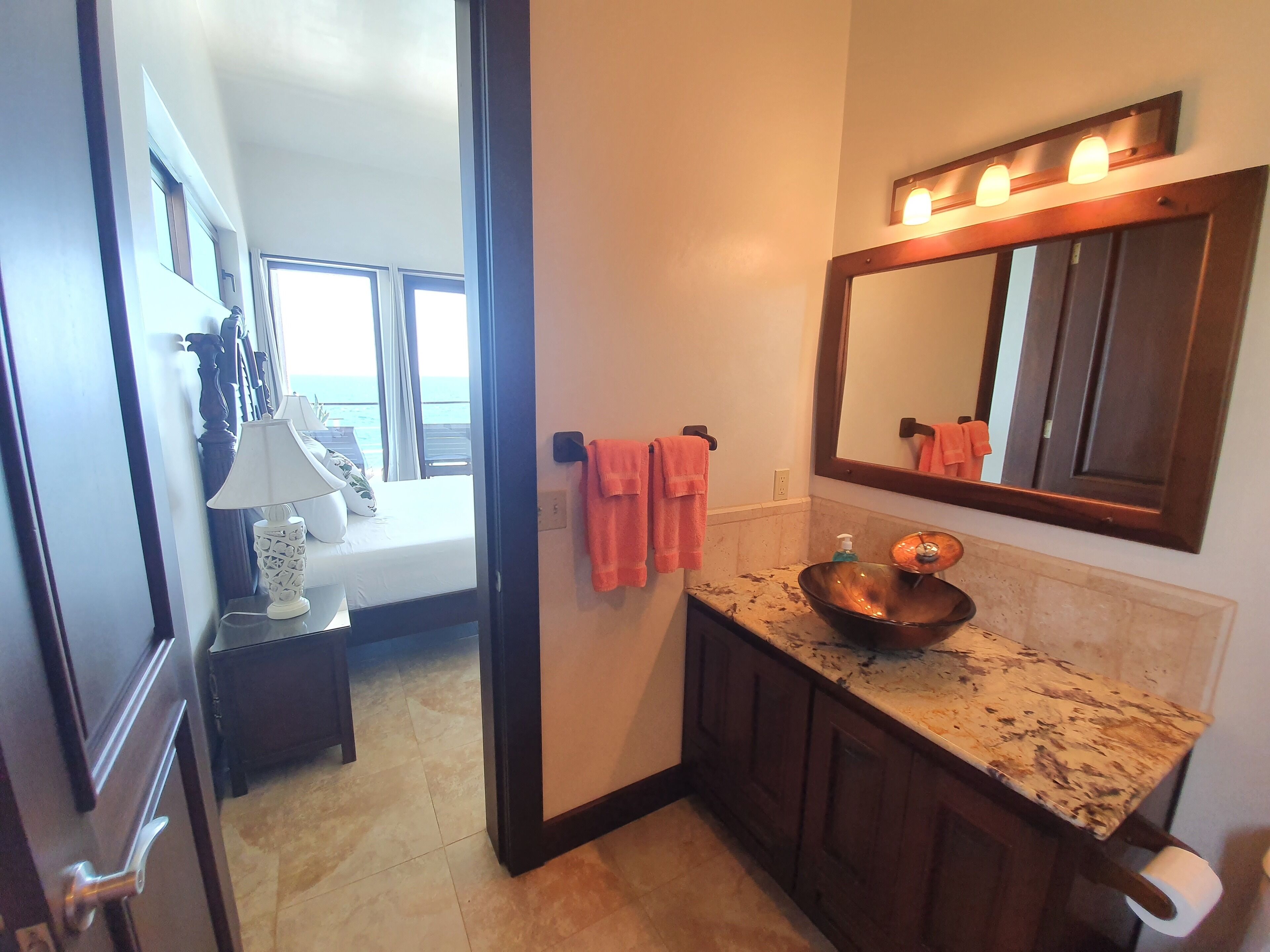 A bathroom with a large mirror, a sink with a copper basin, and a towel rack with pink towels.