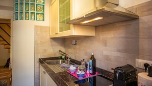 Une cuisine équipée d’un évier en acier inoxydable, d’un four à micro-ondes et d’un grille-pain. Une fenêtre aux vitres vertes et un meuble blanc au-dessus de l’évier complètent l’ensemble.