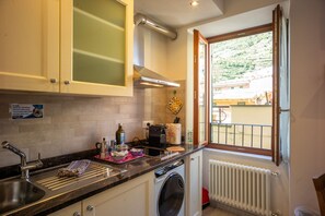 Una cocina con lavadora, ventana con vistas a una ladera y un cartel en la pared.