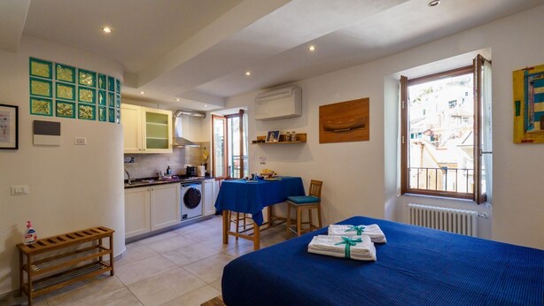 Une chambre avec un lit, une petite table et une chaise. Il y a également un coin cuisine avec des placards et un lave-linge.