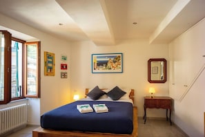 A bedroom with a bed, bedside table, lamp, and a painting on the wall. - Ventu de Ma Second Floor Studio with AC (Vernazza)