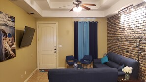 A living room with a sofa, chairs, a TV mounted on the wall, a ceiling fan, and a brick wall. - Chicago Style Town home in a gated community!!Spacious 1100sqft (Edinburg)
