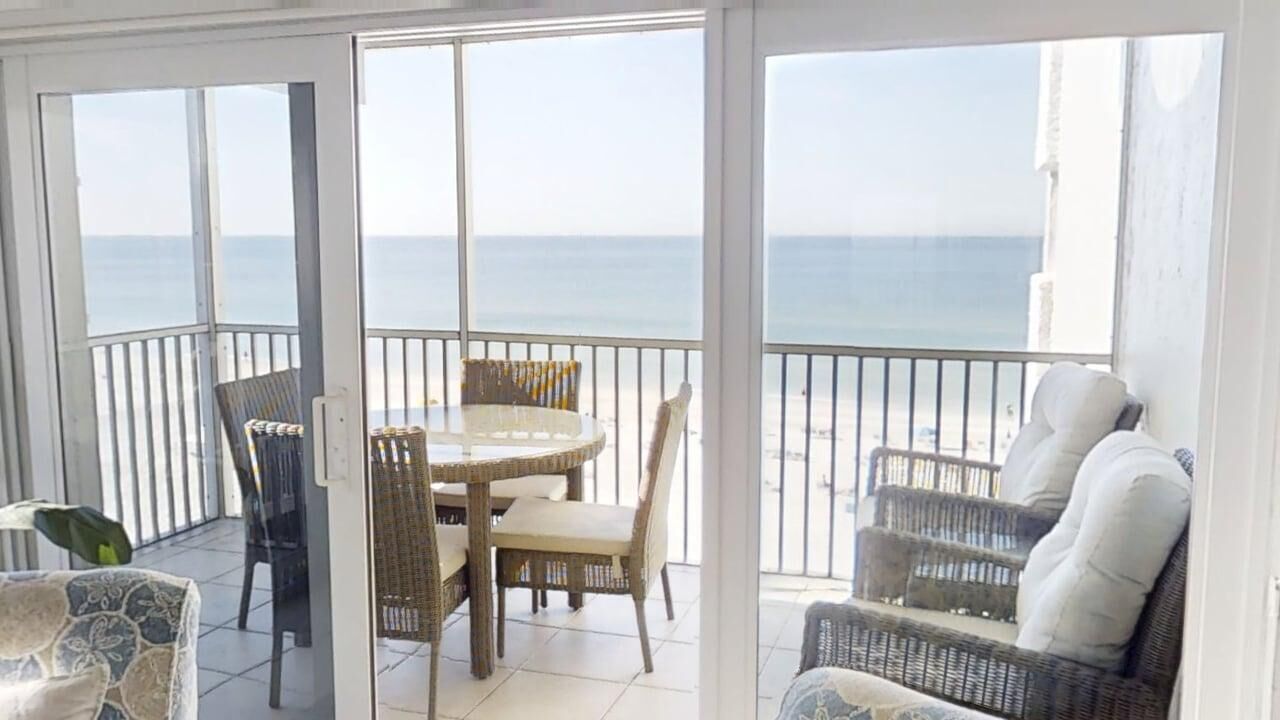 A balcony with a table and chairs, a wicker sofa, and a view of the sea.