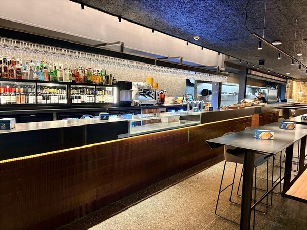 Eine Bar mit einer Theke, Regalen voller Spirituosen und einer Sitzecke mit Tischen und Stühlen.
