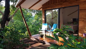 A wooden cabin with a deck, two blue chairs, and a bed visible through a glass door. - Baliyana Lodge (Pinilla)