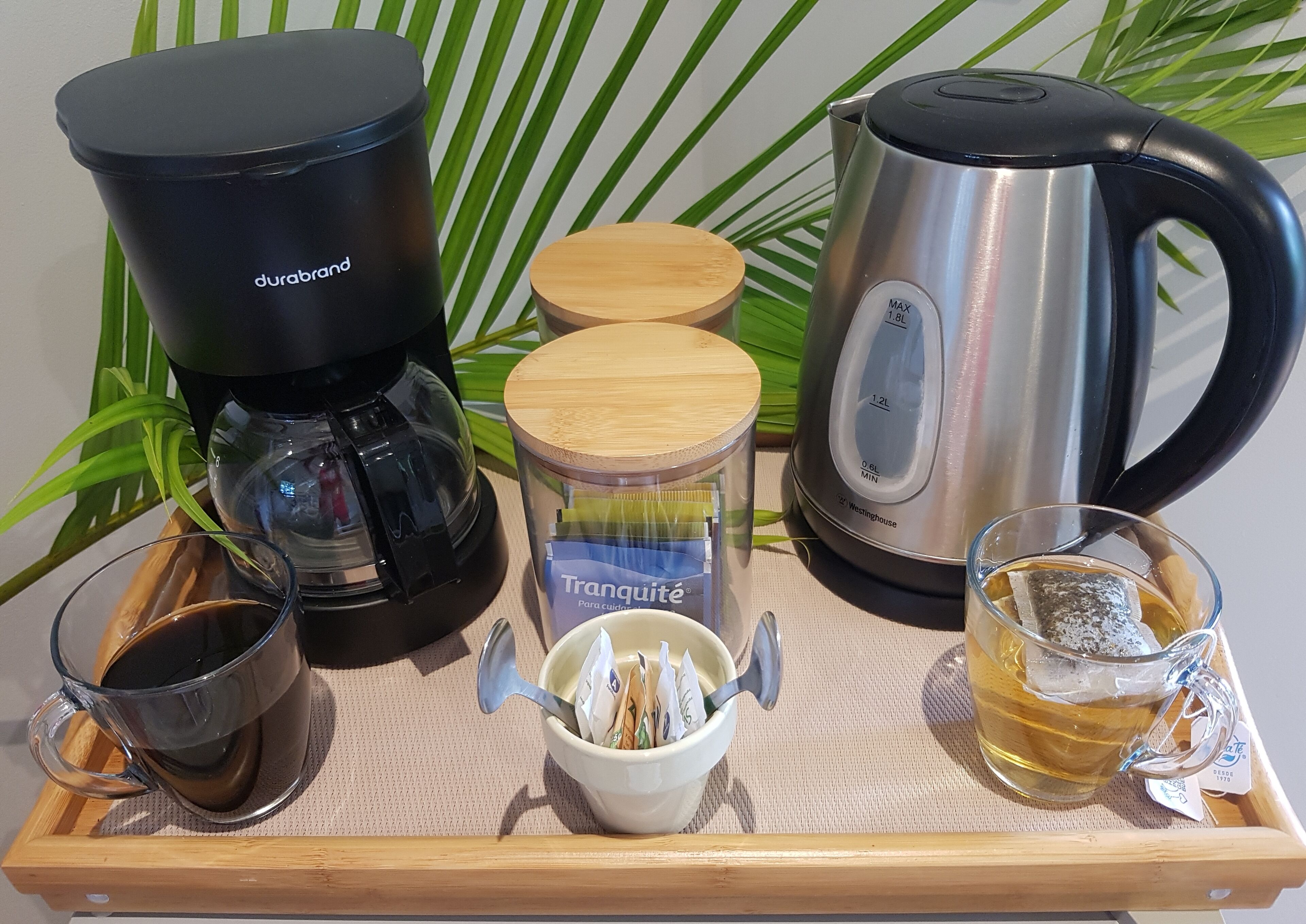 Un plateau contenant une cafetière, une bouilloire, une tasse en verre, une tasse de thé et une boîte de sachets de thé.