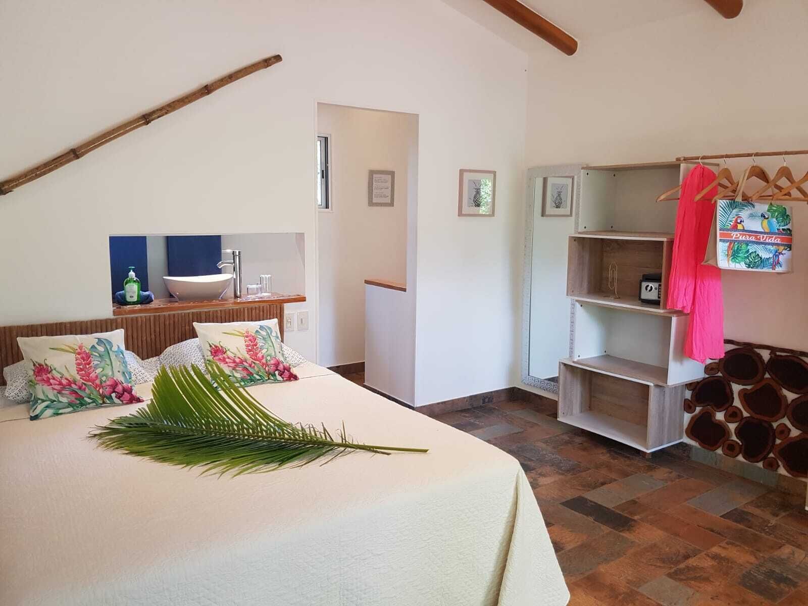 A bedroom with a bed, a bedside table, a mirror, a shelf with a red towel, and a wall with a decorative sign.