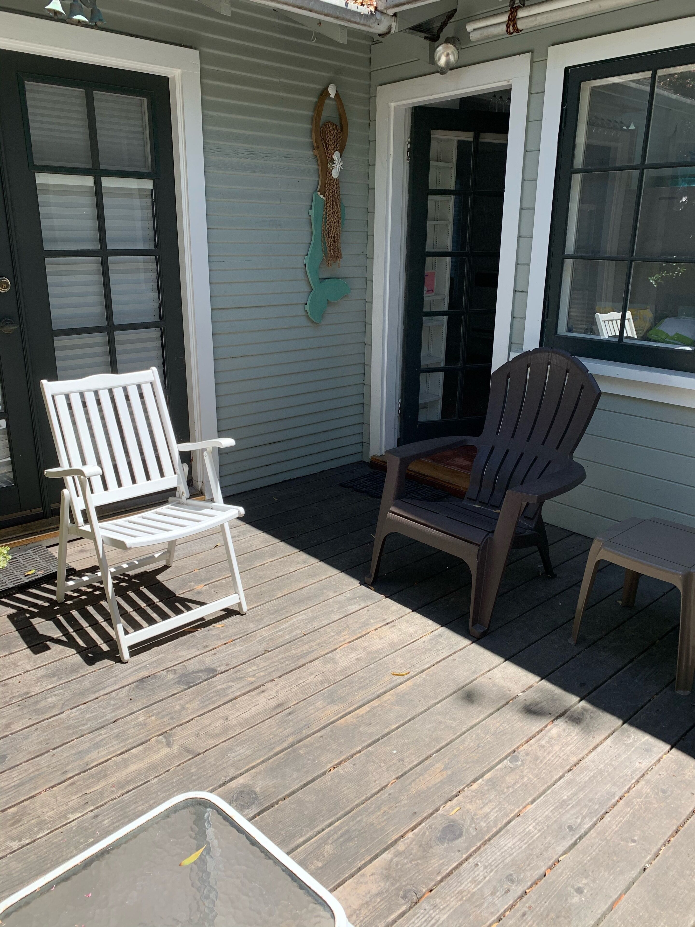 Un espace extérieur abrité, doté d’une terrasse en bois, de deux fauteuils Adirondack et d’une petite table.