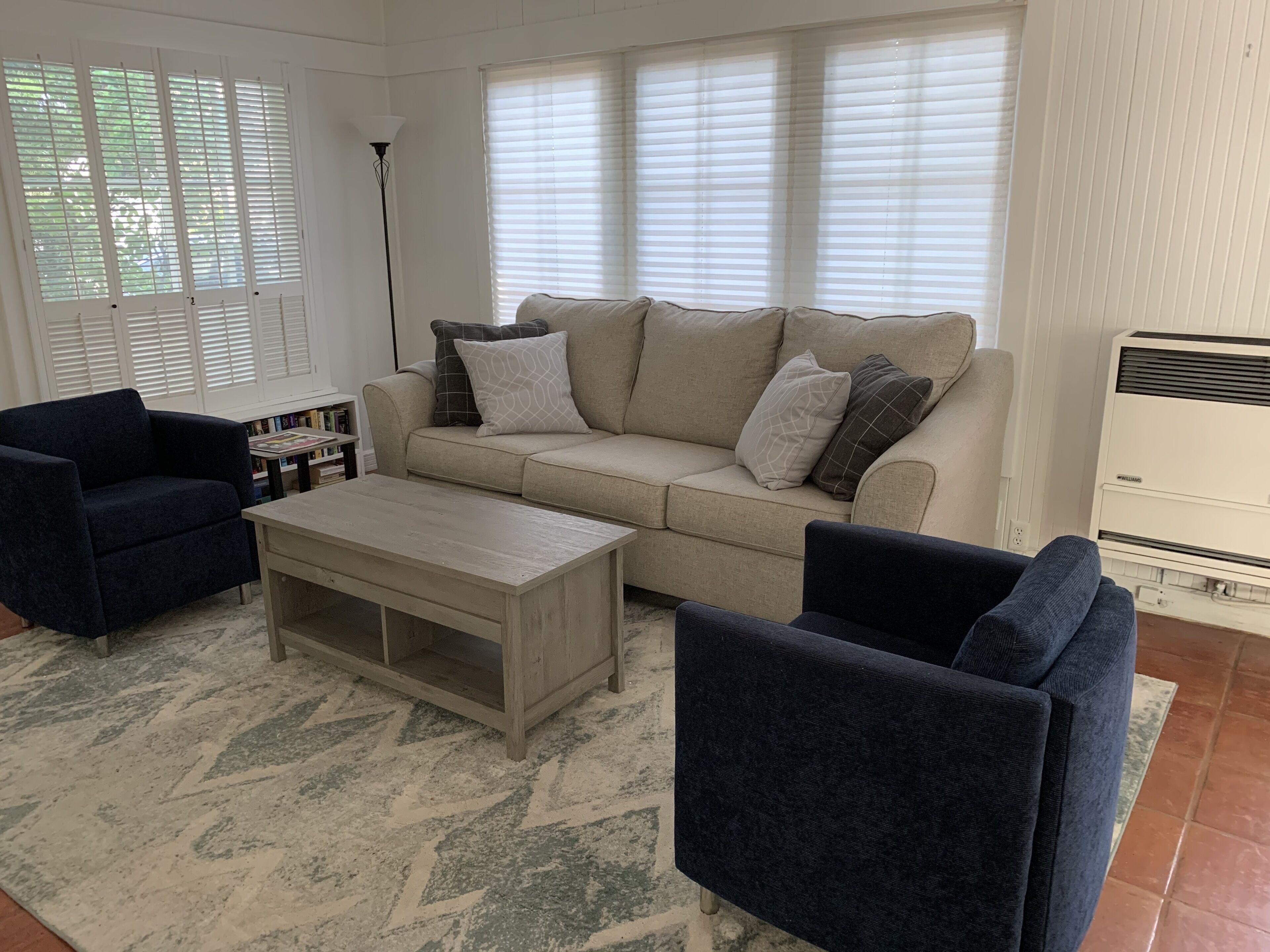 A living room with a beige sofa, two dark armchairs, a wooden coffee table, and a floor lamp.