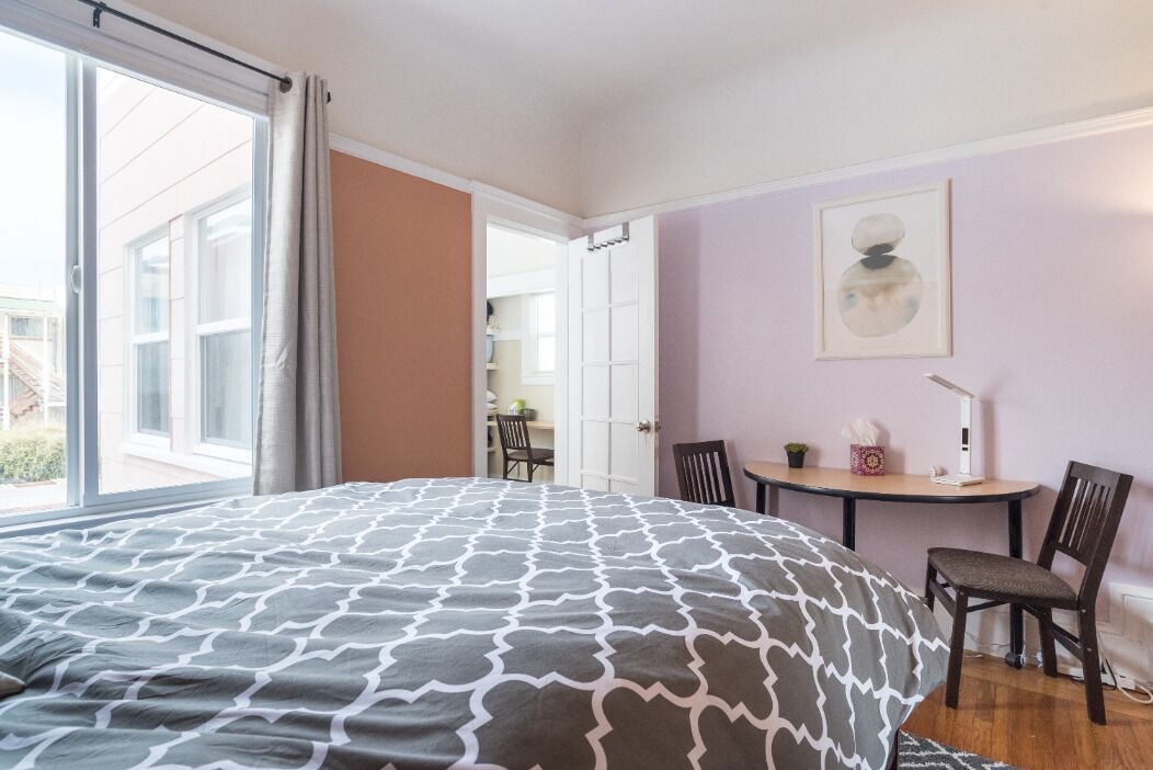 Une chambre avec un grand lit, un bureau, deux chaises et une fenêtre avec des rideaux.