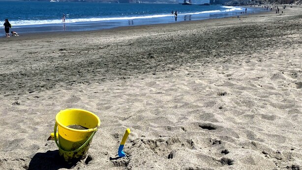 A beach with a yellow bucket and a shovel, a bridge in the background, and people in the distance. - Spacious 3BR Family Flat + Private Garage near Presidio & Beach (SF)