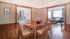 A dining area with a wooden table and chairs, a chandelier, framed pictures on the walls, and a view to a living room with a sofa and a window. - Spacious 3BR Family Flat + Private Garage near Presidio & Beach (SF)