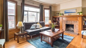A cozy living room with a fireplace, a sofa, a coffee table, and a bookshelf. - Spacious 3BR Family Flat + Private Garage near Presidio & Beach (SF)