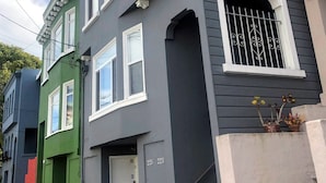 A two-story building with a dark gray facade, white trim around windows and doors, and a small balcony with potted plants. - Spacious 3BR Family Flat + Private Garage near Presidio & Beach (SF)
