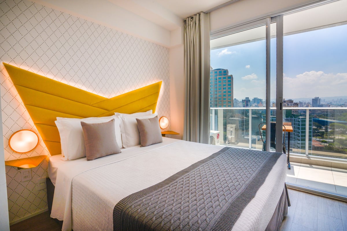 A hotel room with a large bed, a city view, and a modern design.