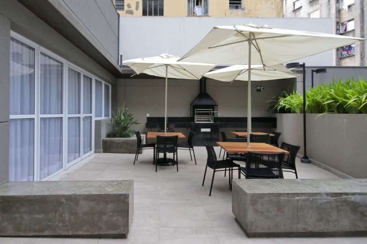 An outdoor patio with tables and chairs, umbrellas, and a grill area.