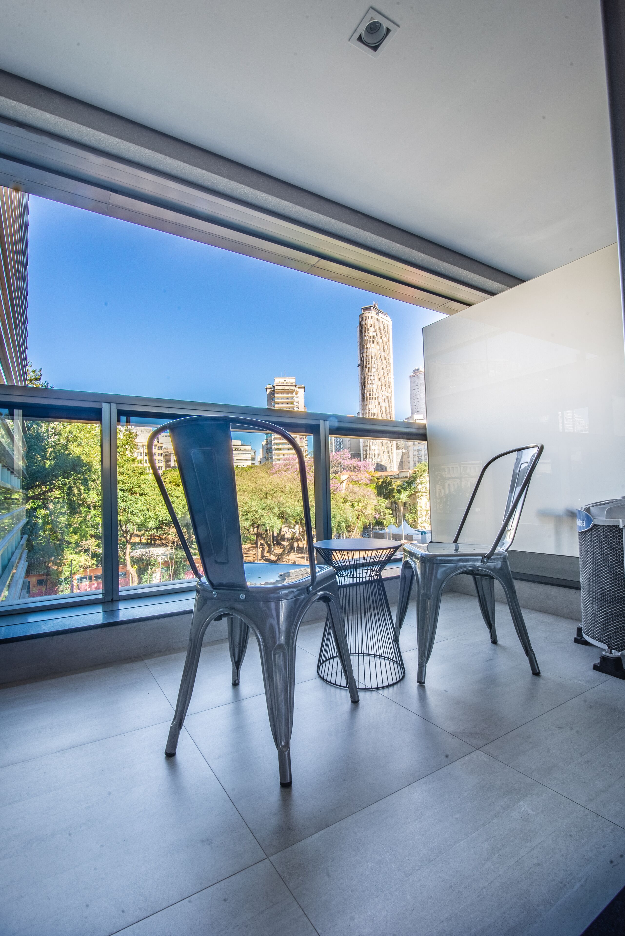A balcony with two chairs and a table, overlooking a cityscape with buildings and trees.