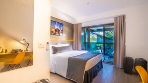 A modern hotel room with a large bed, a desk with a chair, a window with a view of greenery, and a balcony. - 360 República (São Paulo)