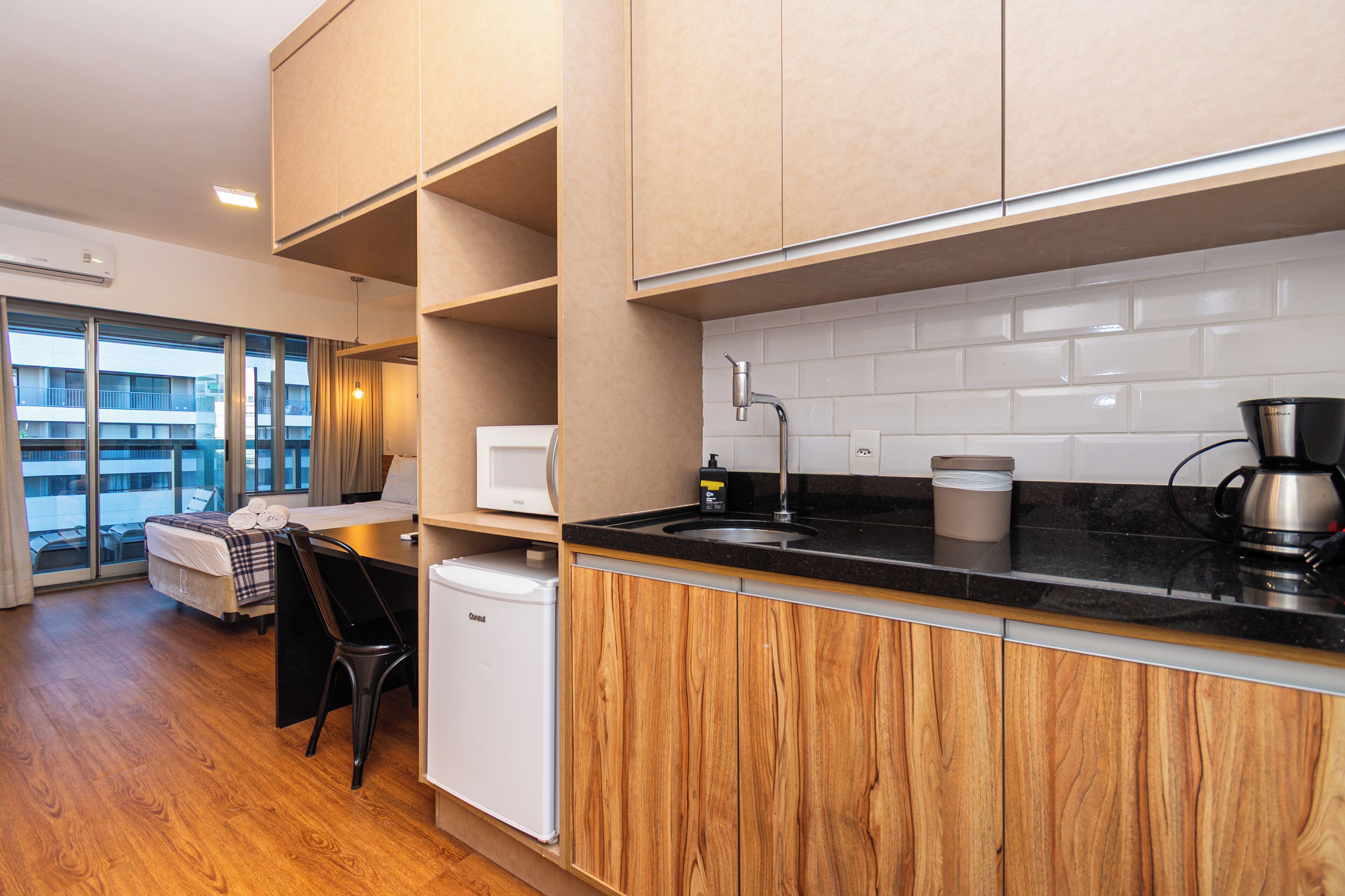 A modern kitchen with wooden cabinets, a black countertop, and a view of a balcony.